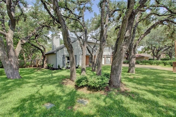 A house surrounded by large trees with a well-maintained lawn.