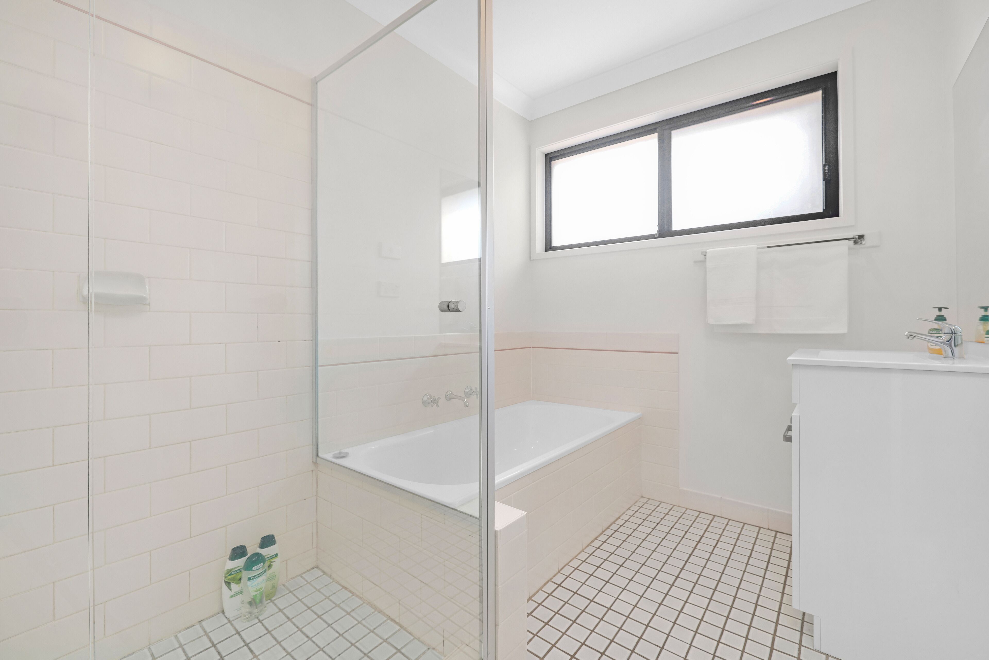 Un bany modern amb una dutxa envidriada, una banyera blanca i un petit finestral sobre el lavabo.