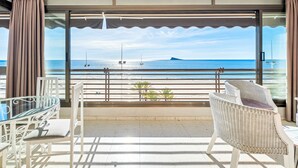 Un balcon avec une table et des chaises en verre, une vue sur la mer et une île au loin.