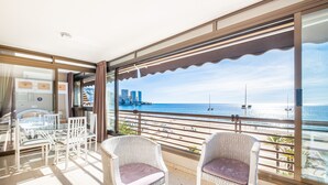 Un balcon avec des fauteuils en osier, une table en verre et une vue sur l’océan et le paysage urbain.