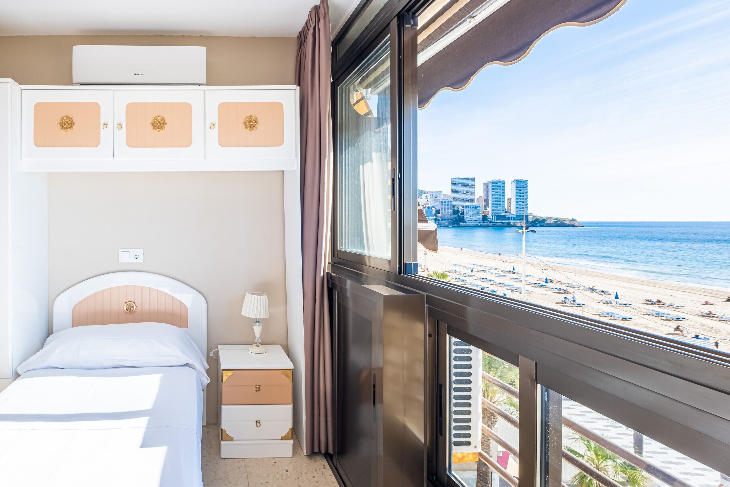 Ein Hotelzimmer mit Bett, Schminktisch, Nachttisch und Fenster mit Blick auf Strand und Stadt.