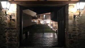 Une entrée rustique en pierre menant à une maison de campagne, avec un plancher en bois et deux lanternes fixées aux murs.
