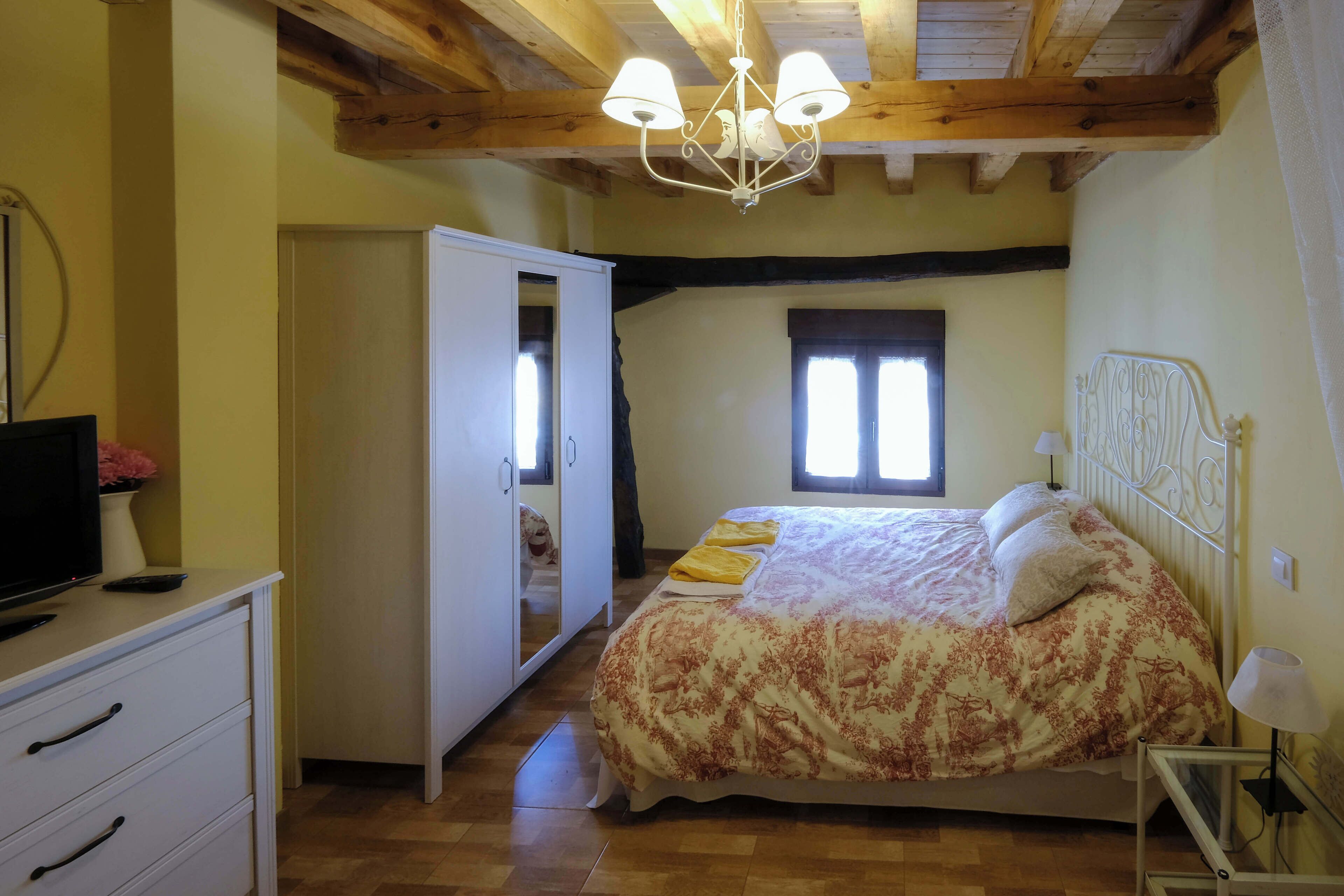 A bedroom with a bed, a TV, a wardrobe, and a mirror.