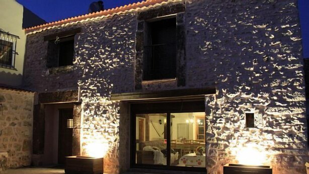 Un bâtiment en pierre avec un toit en tuiles, une porte en bois et deux fenêtres illuminées.