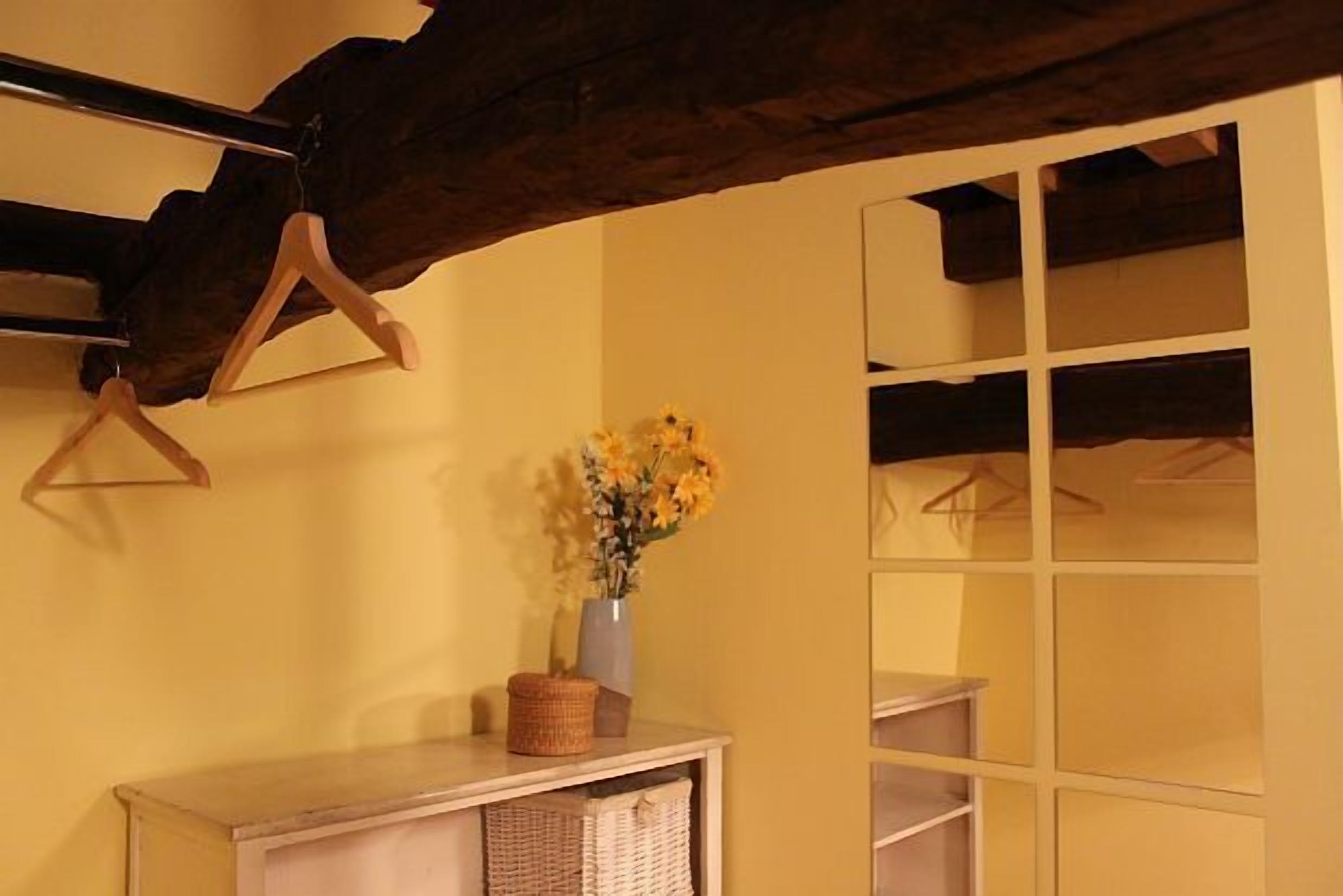 Ein Zimmer mit Holzbalkendecke, einem Tisch mit Blumen in einer Vase und einem Spiegel an der Wand.