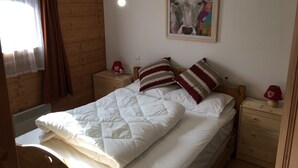 A cozy room with a wooden bed, a nightstand with a lamp, and a painting on the wall. - Spacious 3 Bedroom Apartment Right on the Slopes (Les Esserts, Morillon)
