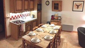 A compact kitchen with wooden cabinets, a stove, and a dining table set for four. - Spacious 3 Bedroom Apartment Right on the Slopes (Les Esserts, Morillon)