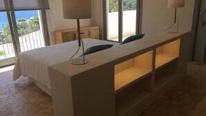 A modern bedroom with a large bed, a bedside table with lamps, and a view of the sea through large windows. - Wonderful luxury villa in 1st line of the sea in Moraira with private pool. (Teulada / Moraira)