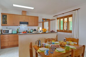 A kitchen with wooden cabinets, a microwave, and a dining table set with plates, cups, and a pitcher. - Cosy Front-Line Beach Apartment in Mallorca Up To 6 Guests (Son Serra de Marina)