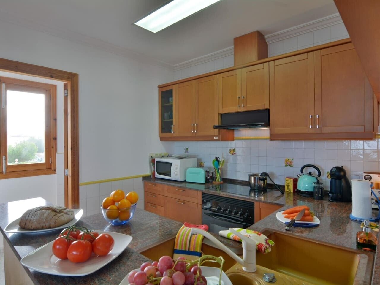 Une cuisine avec des meubles de rangement en bois, un four à micro-ondes, un grille-pain et divers fruits et légumes disposés sur le plan de travail.