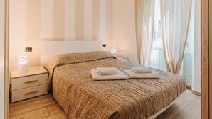 A neatly made bed with a striped headboard, a bedside table with a lamp, and a window with curtains. - I FRAGOLI A SANTA CROCE (Firenze)