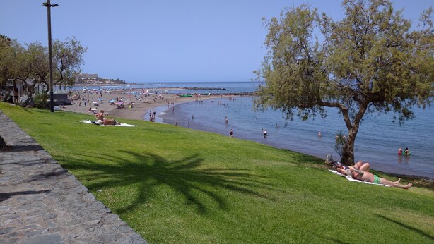A beach with people sunbathing, swimming, and walking along the shore.