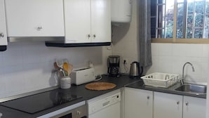 A compact kitchen with white cabinets, a black countertop, a coffee maker, and a dish rack.