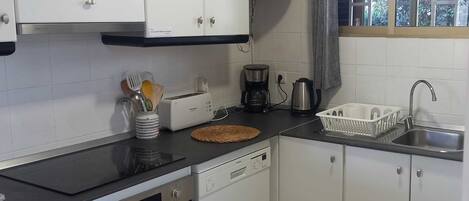Una cocina compacta con armarios blancos, encimera negra, cafetera y escurreplatos.