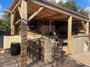 A wooden outdoor bar area with a stone oven, bar stools, and a Guinness sign.