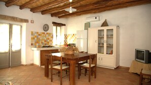 A kitchen with wooden beams, a tiled backsplash, a dining table with chairs, a white cabinet, and a television on a table. - DomusAntiga three-room apartment 10 minutes from the most beautiful beaches of the coast!Wifi (San Giovanni Suergiu)