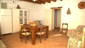 A dining area with a wooden table and chairs, a white refrigerator, and a cabinet with glass doors. - DomusAntiga three-room apartment 10 minutes from the most beautiful beaches of the coast!Wifi (San Giovanni Suergiu)