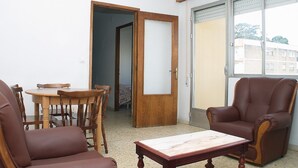 A living room with a wooden table, two leather chairs, a sofa, and a sliding glass door leading to a balcony.