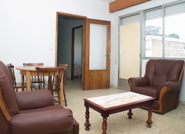 A living room with a wooden table, two leather chairs, a sofa, and a sliding glass door leading to a balcony.