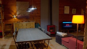 L’intérieur chaleureux d’un chalet comprend une table à manger, des chaises, un canapé, un téléviseur et un poêle à bois.