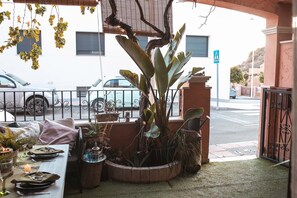 Zona de menjador amb taula preparada per a dues persones, envoltada de plantes en testos i una petita font.