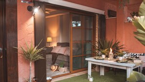 A cozy outdoor seating area with a table set for dining, surrounded by potted plants and a sliding glass door leading to a room with a bed and a lamp. - Apartment La Invencible Terreros in 1st line of beach (San Juan de los Terreros)