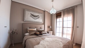 A bedroom with a large bed, a chandelier, a bedside table, a lamp, a vase with flowers, and a window with curtains. - Apartment La Invencible Terreros in 1st line of beach (San Juan de los Terreros)