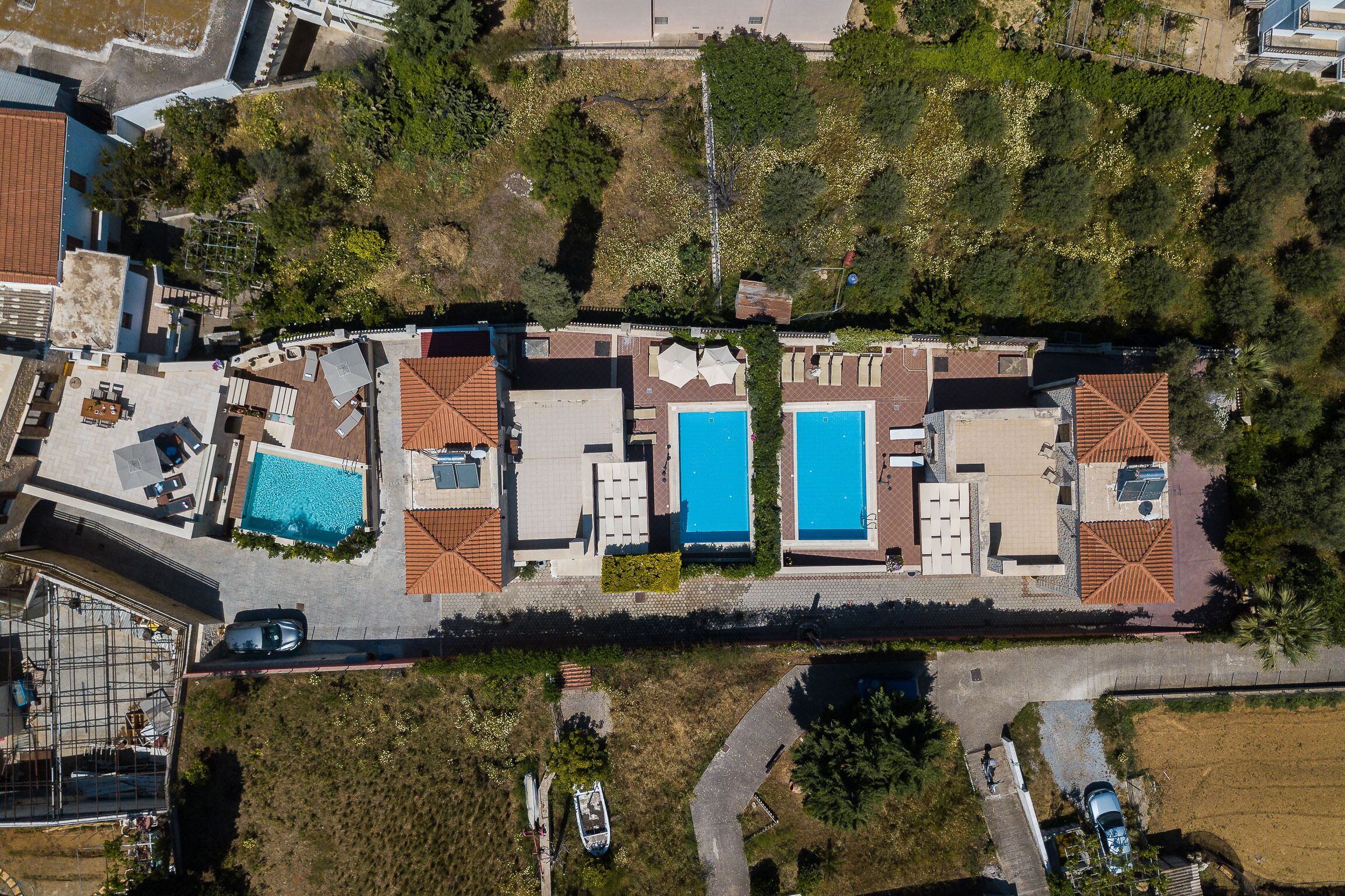 An aerial view of a hotel with multiple swimming pools, a covered outdoor area, and a parking lot.