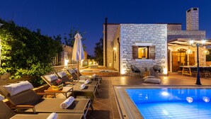 Un espace aménagé au bord de la piscine, avec des chaises longues, une piscine et un bâtiment en pierre doté d’une cheminée.