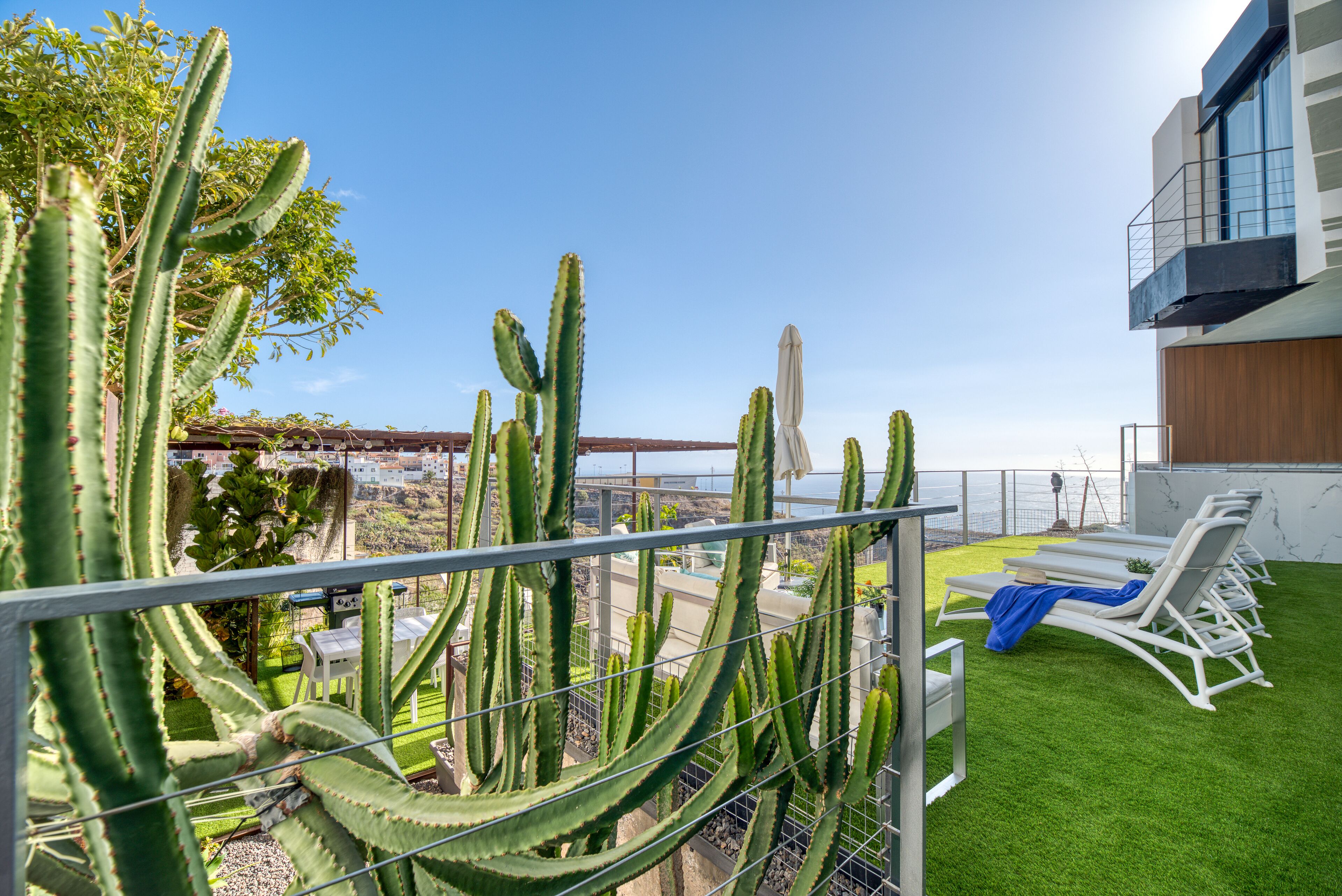 A rooftop terrace with a view of the sea, featuring cacti, a pool, and lounge chairs.