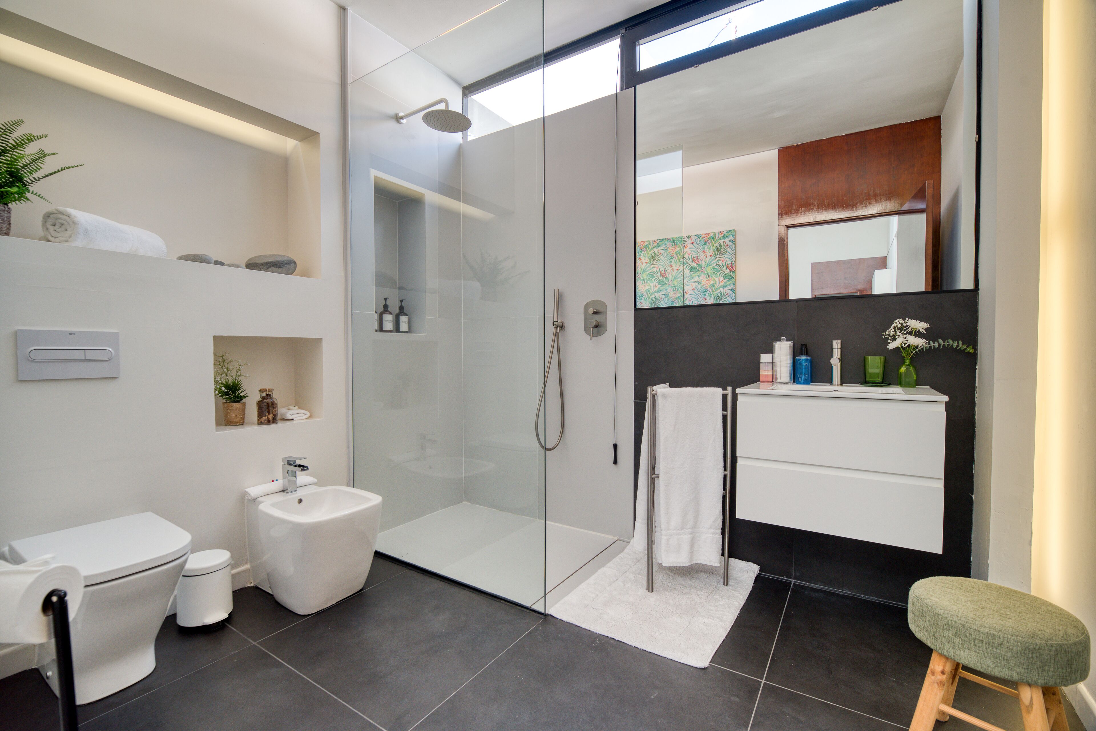 A modern bathroom with a glass shower enclosure, a white vanity, and a green stool.