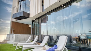 A modern building with a glass facade, outdoor lounge chairs, and a small garden area. - LAST MINUTE -  Design villa, climatized pool, sea views 6 pers. (Tijoco Bajo)