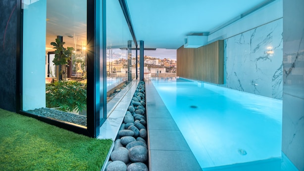 A modern indoor pool with clear glass walls, a stone-lined pathway, and a view of the cityscape. - LAST MINUTE -  Design villa, climatized pool, sea views 6 pers. (Tijoco Bajo)