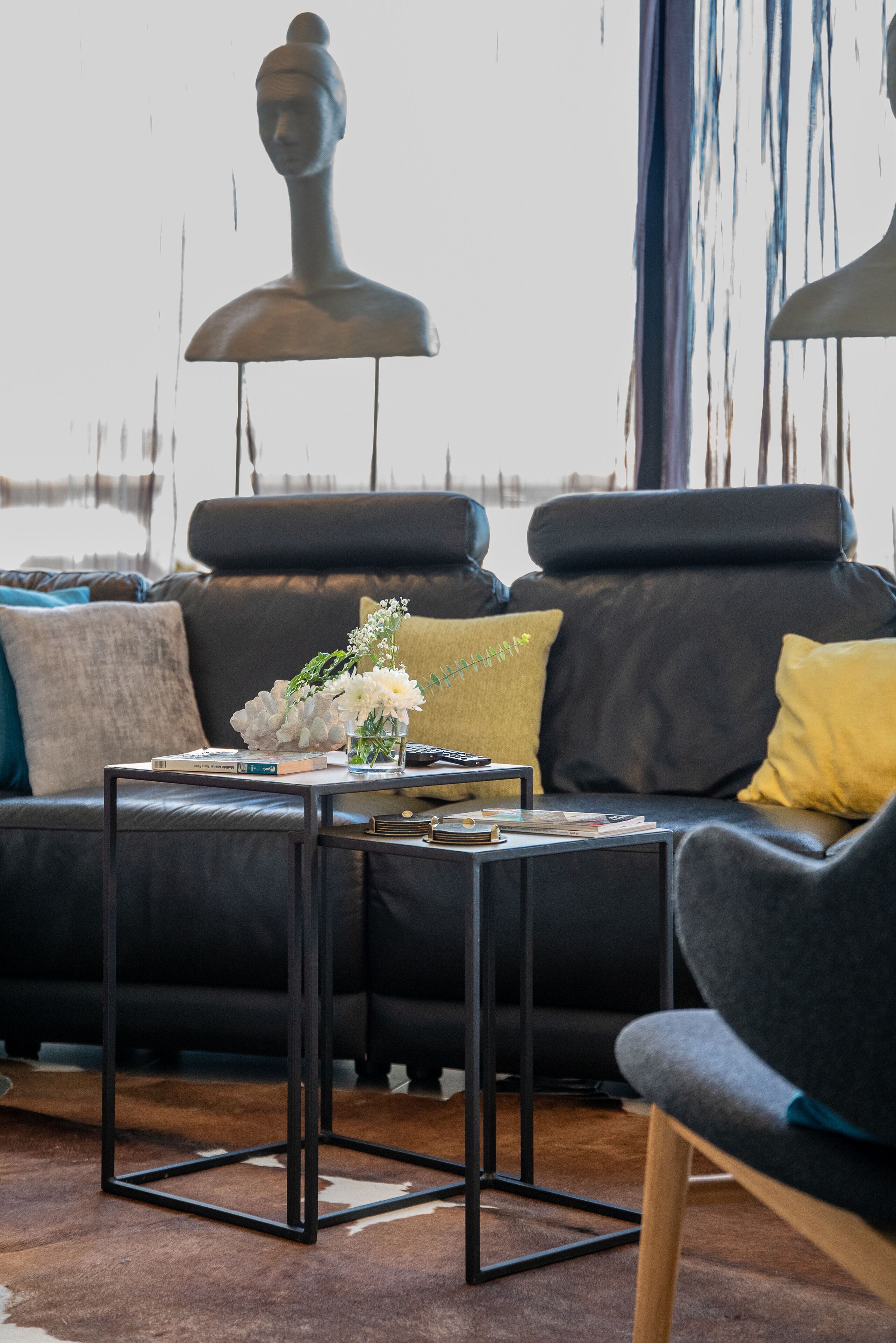 A modern living room with a black leather sofa, a glass coffee table, and a decorative bust sculpture.