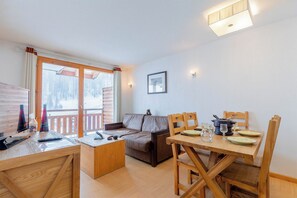 Une pièce chaleureuse avec une table à manger en bois, mise pour deux personnes, un canapé et un bureau avec un ordinateur et une bouteille.