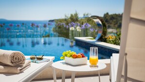 A poolside setting with a table, a bowl of fruit, a glass of orange juice, and a rolled towel. - Villa Argemonia – Luxury Beachfront Escape in Tatinje Bay (Okrug Gornji)