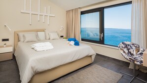 A hotel room with a large bed, a view of the sea, a modern chair, and a decorative wall piece. - Villa Argemonia – Luxury Beachfront Escape in Tatinje Bay (Okrug Gornji)