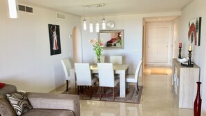 Una sala de estar moderna con sofá, mesa de comedor y sillas. Hay un espejo sobre la mesa y un reloj en la pared.