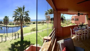 Un balcón con vista a una piscina, palmeras y una playa distante.