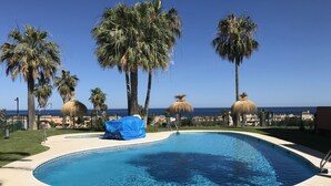 Una piscina con vista despejada al océano, rodeada de palmeras y una estructura con techo de paja.