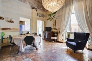 Zona pranzo con tavolo apparecchiato per due, una poltrona nera e un grande lampadario.