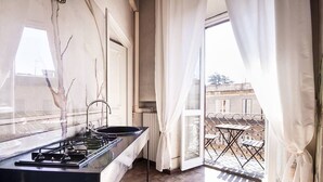 Una cocina con estufa a gas, un lavamanos y vistas al balcón exterior.