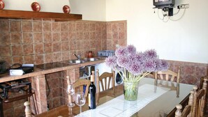 A kitchen with a tiled backsplash, a sink, and a dining table with chairs. There is a vase with flowers on the table.