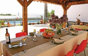 An outdoor dining area with a table set for two, featuring a bottle of wine, glasses, a bowl of fruit, and a vase of flowers.