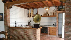 A kitchen with a brick island, wooden beams, a gramophone, and tiled walls.