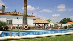 A swimming pool with a tiled deck, palm trees, and a gazebo.