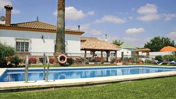 Una piscina con borde de baldosas, palmeras y un pabellón.