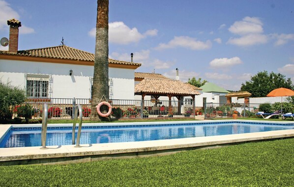 A swimming pool with a tiled deck, palm trees, and a gazebo.