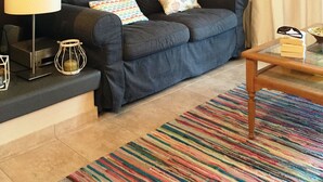 A living room with a dark sofa, a glass coffee table, a colorful striped rug, a framed picture on the wall, and a lamp. - Seafront apartment ΙΙ in Kiveri, near Nafplion. (kiveri)