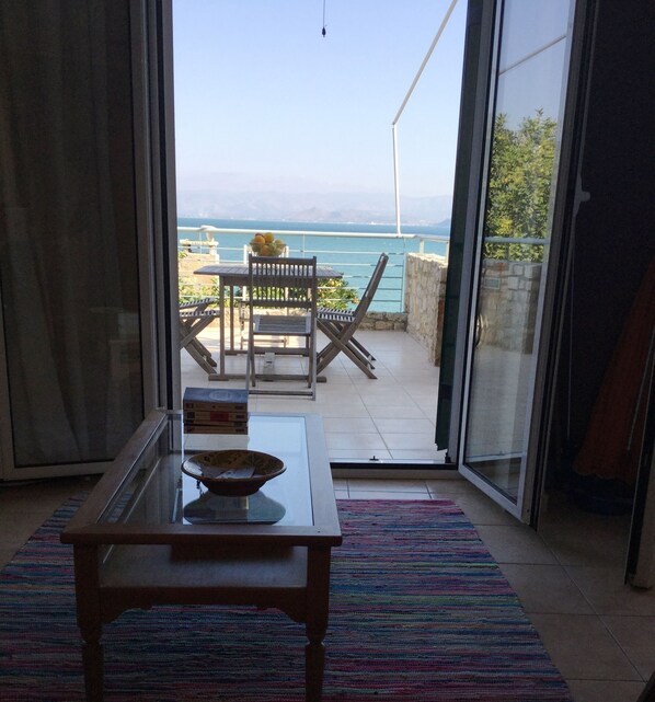 A room with a view of the sea, a table with a bowl, and a chair.